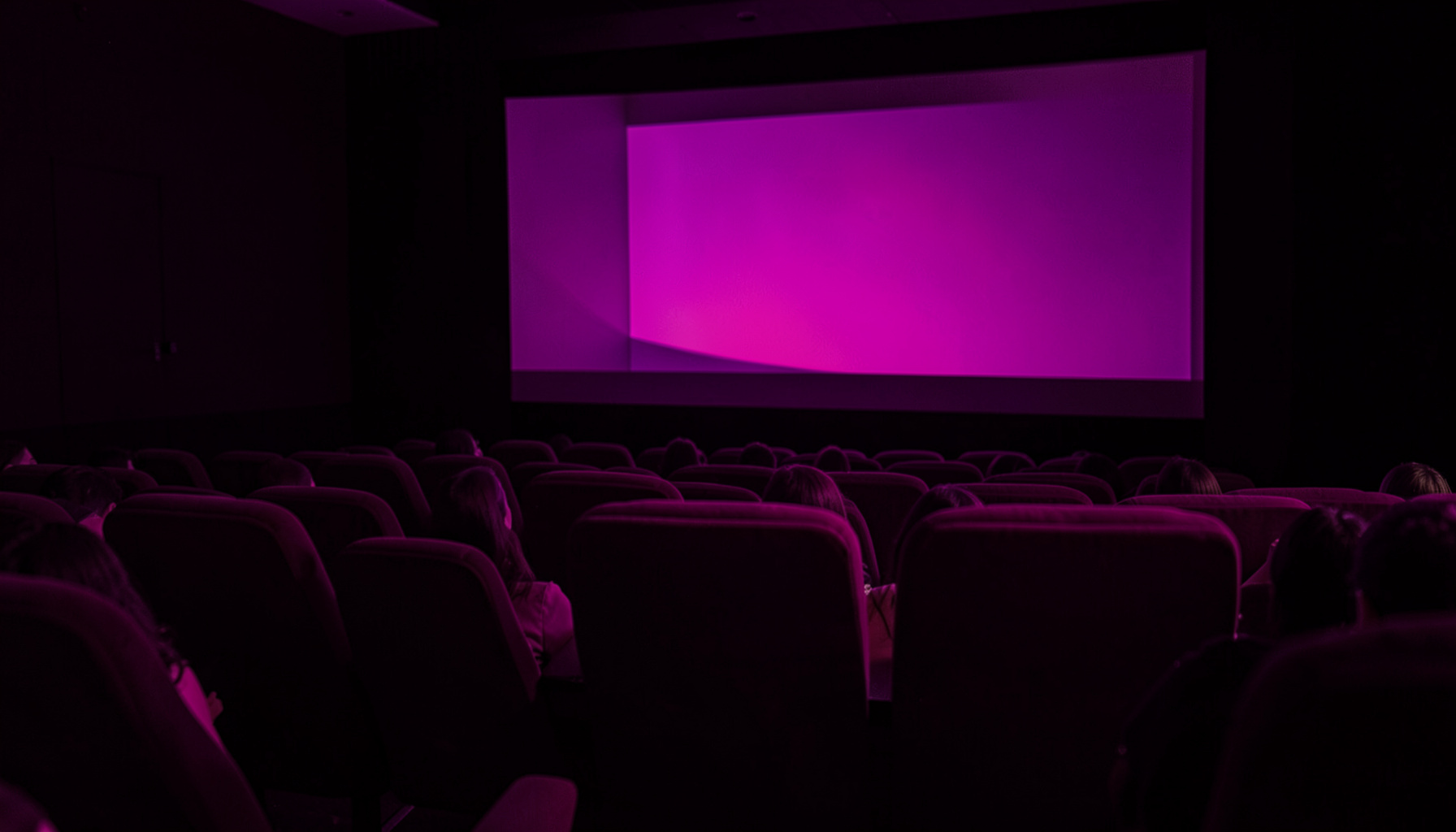 Sala de cine en penumbra con butacas rojas y pantalla iluminada, atmósfera violeta y dorada