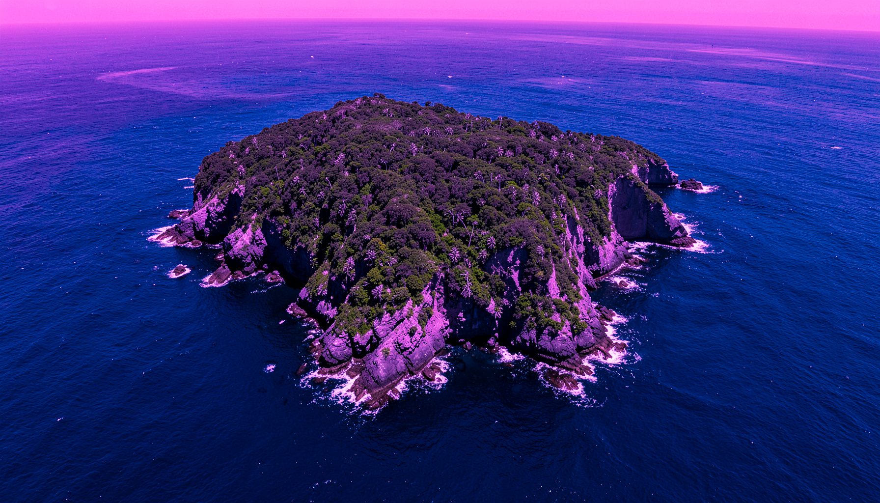 Vista aérea de una isla selvática rodeada por aguas azul profundo, con acantilados verdes que caen abruptamente sobre el océano Pacífico.