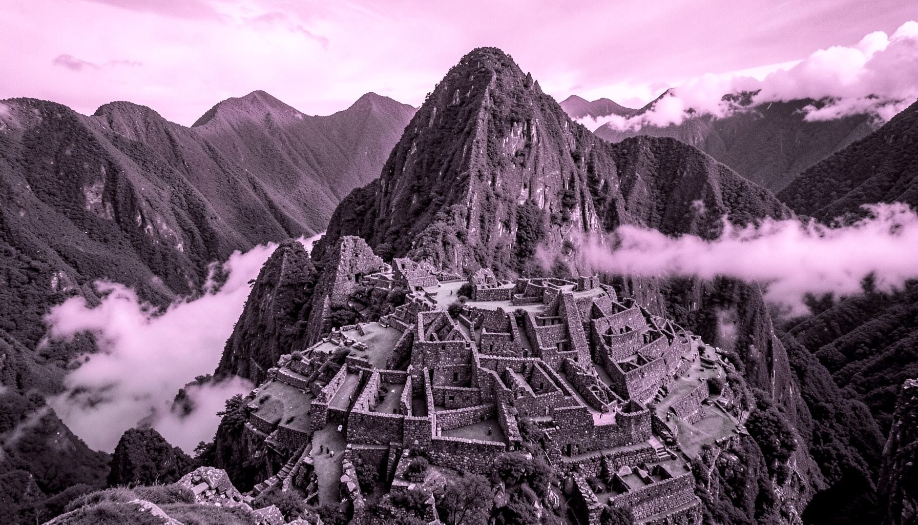 Ciudadela inca de piedra enclavada entre montañas verdes y picos escarpados, con nubes bajas rozando las terrazas milenarias.