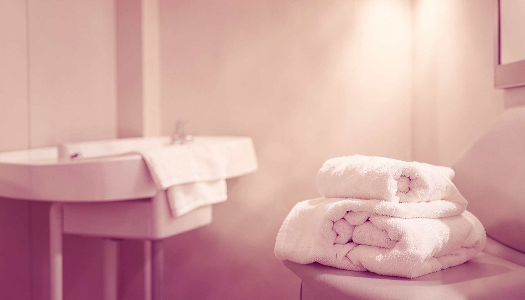Ambiente sereno de cabina de estética con toallas blancas enrolladas, luz cálida y difusa, tonos crema y beige.