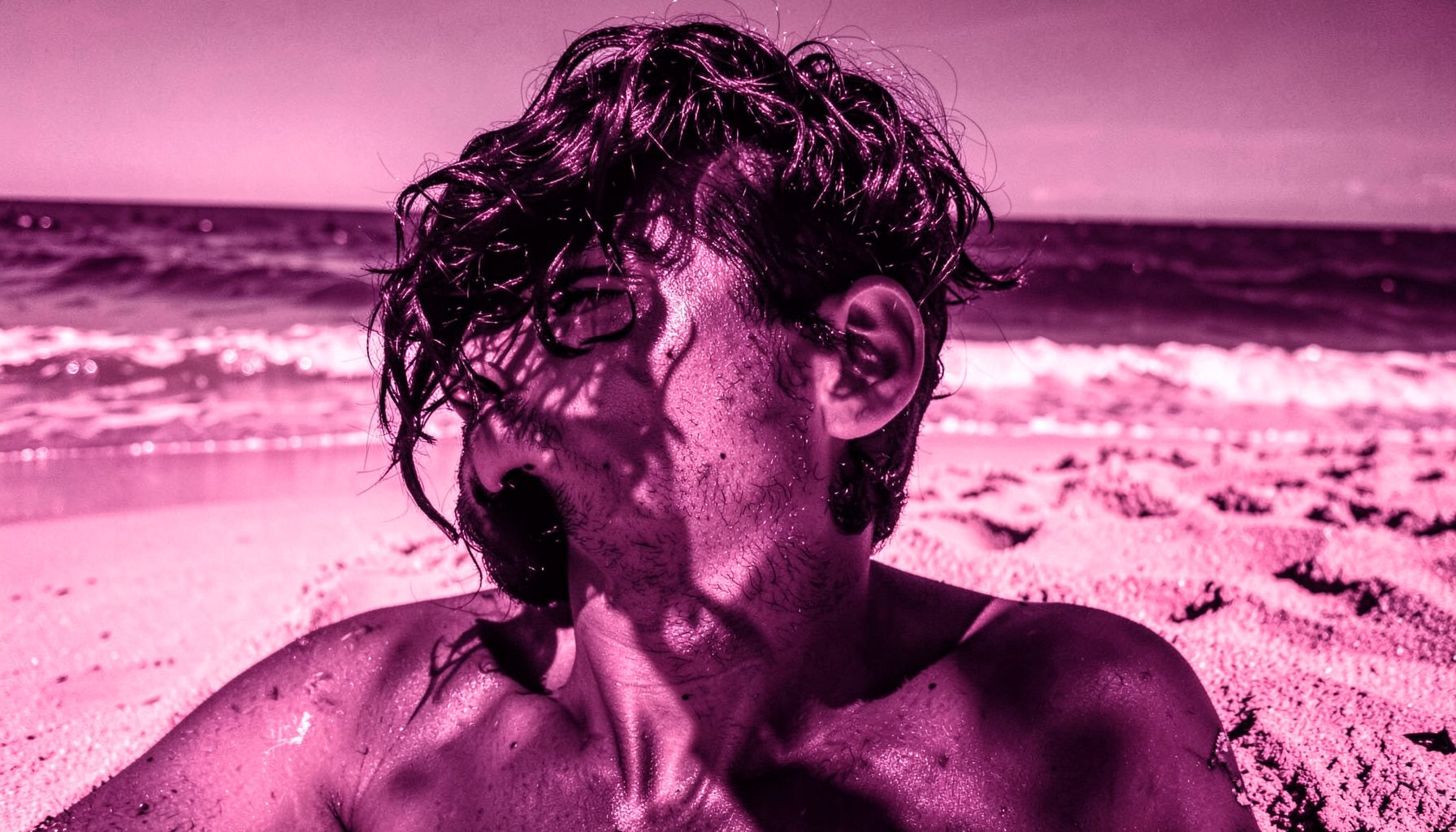 Cabello oscuro y brillante al sol junto a una playa de arena dorada, con reflejos cálidos de luz natural.