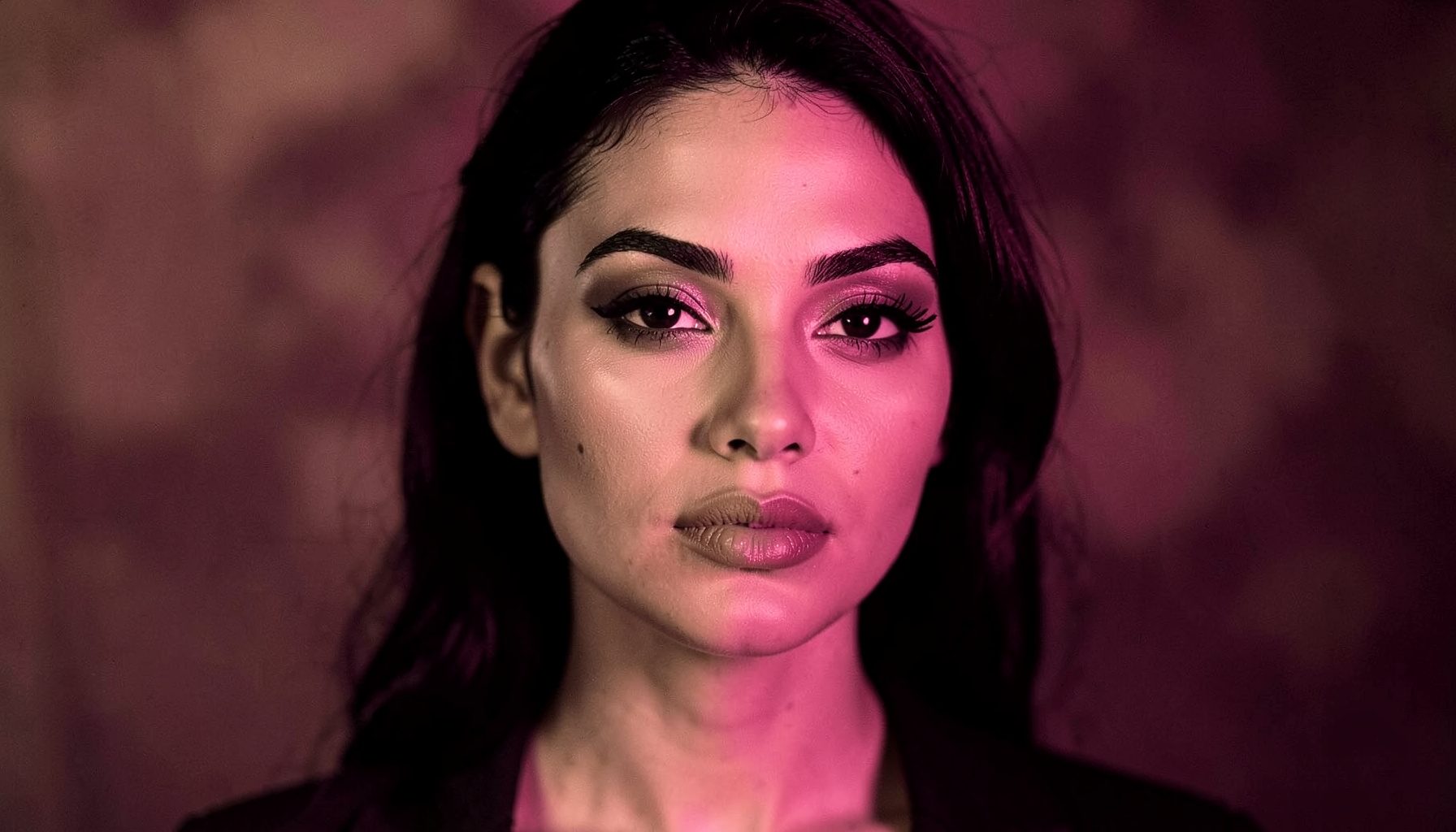 Retrato en claroscuro de una mujer latina con maquillaje impecable en tonos tierra, fondo difuminado en sombras cálidas.
