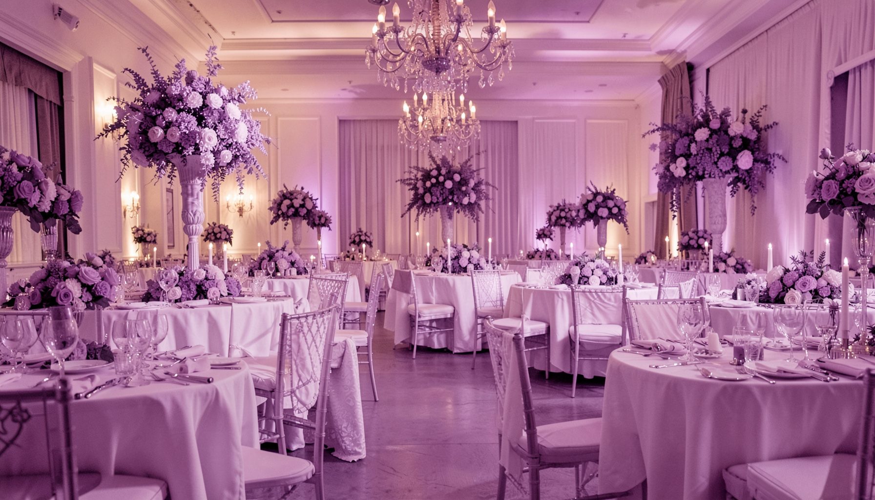 Salón de eventos con mantelería blanca, arreglos florales en tonos lavanda y luz ambiental dorada.