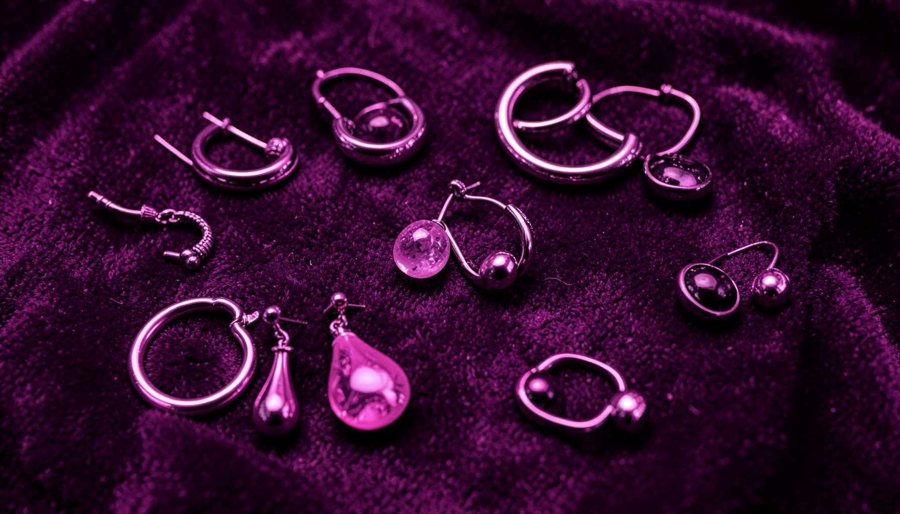 Colección de aretes de distintos diseños —argollas, gotas y botones— dispuestos sobre terciopelo morado oscuro.
